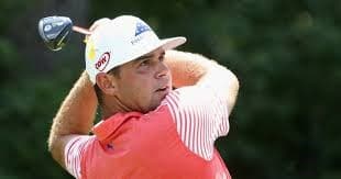 Gary Woodland after his swing with a white hat and red shirt with stripes